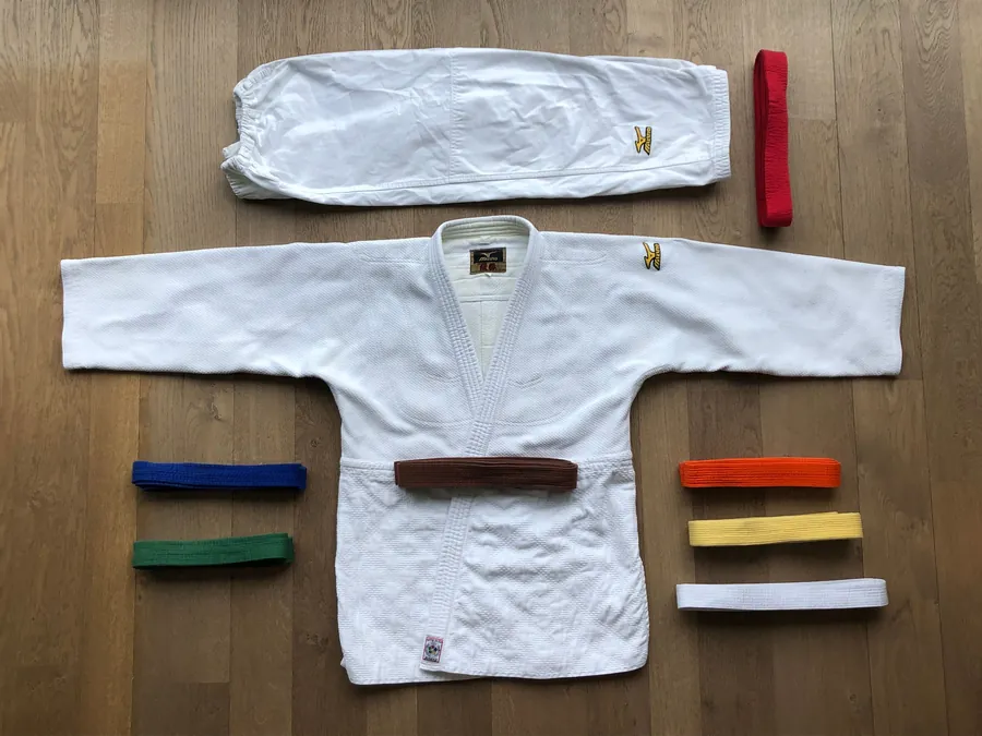 A white karate gi laid flat next to a row of coloured belts