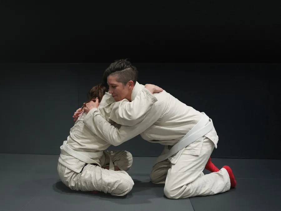 Two adults in gis grappling on a dark mat