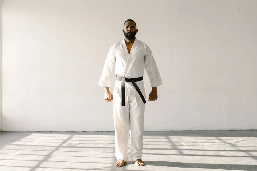 A black belt instructor in a white gi stands in a sunlit studio