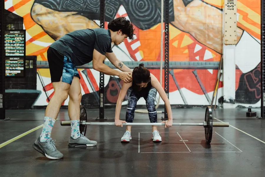 A coach guides a woman through a barbell deadlift setup