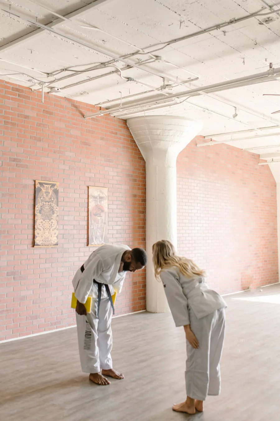 Two students in gis bow to each other in a bright, brick-walled training room